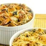 Two white ramekins filled with baked cheesy bread pudding with spinach on a wooden surface.