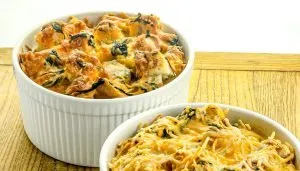 Two white ramekins filled with baked cheesy bread pudding with spinach on a wooden surface.