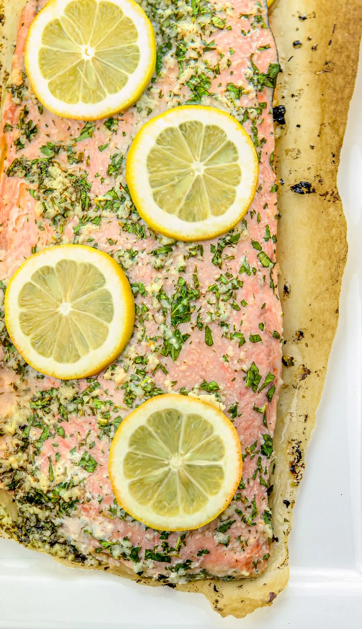 Salmon fillet seasoned with herbs and garlic, topped with lemon slices on parchment paper.