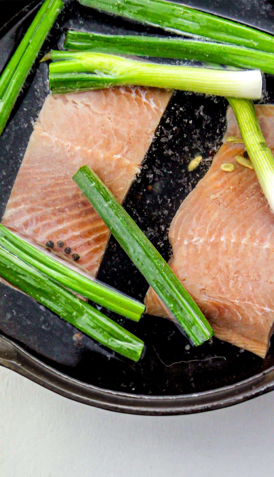 Raw salmon fillets and green onions in a black cast iron skillet.