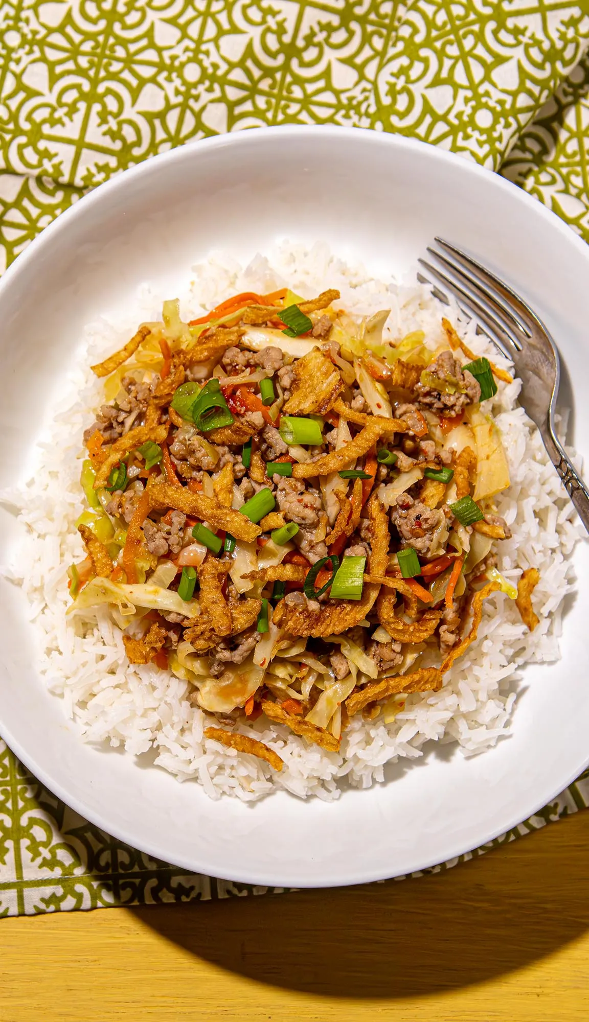 White rice topped with ground meat, cabbage, carrots, fried onions, and chopped green onions in a white bowl with a fork on the side.