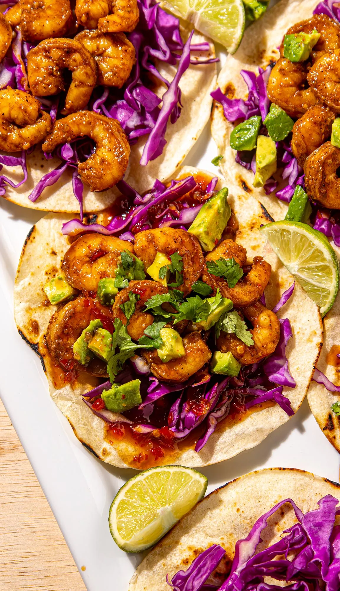 Spicy shrimp tacos with purple cabbage, avocado chunks, cilantro, and lime wedges on toasted tortillas.
