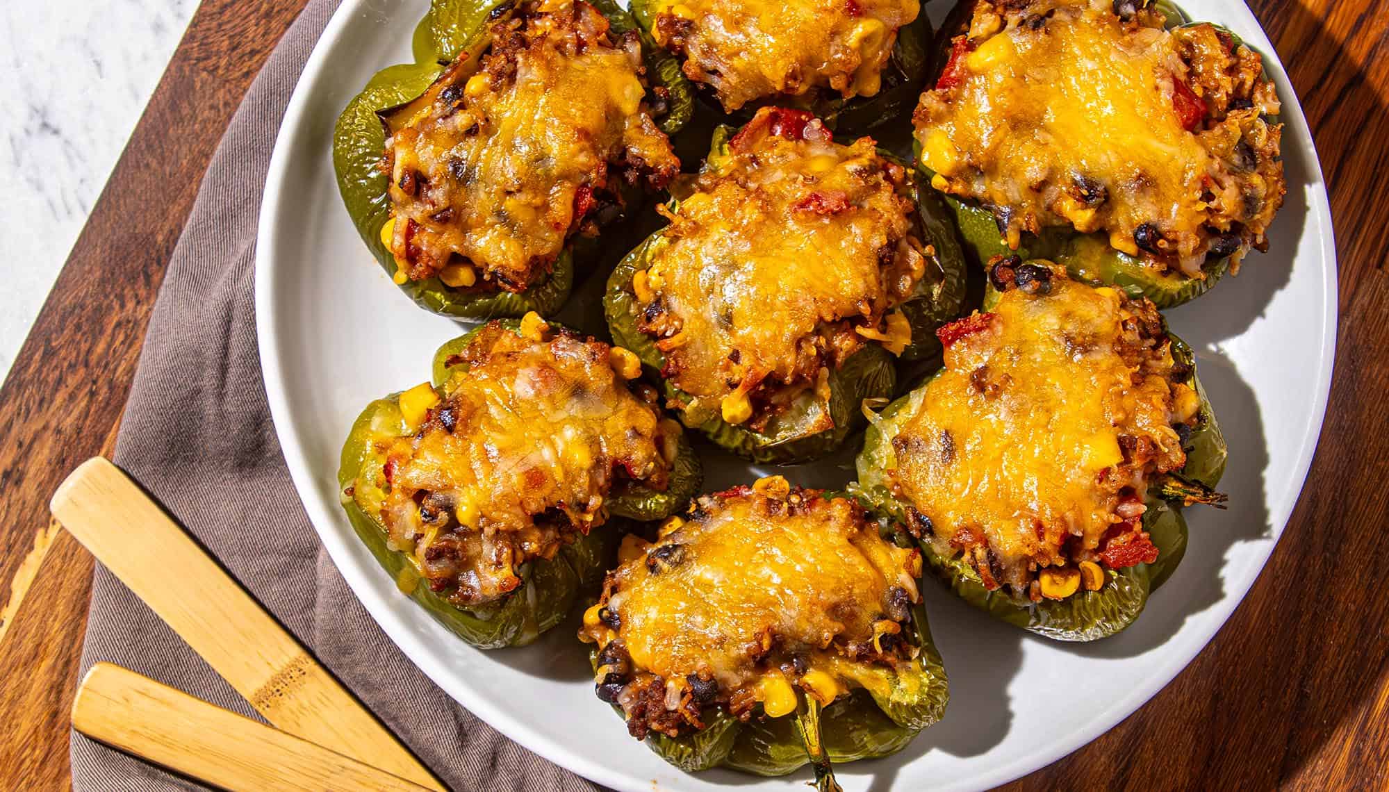 Green bell peppers stuffed with a mixture of rice, black beans, corn, tomatoes, and melted cheddar cheese on a white plate.