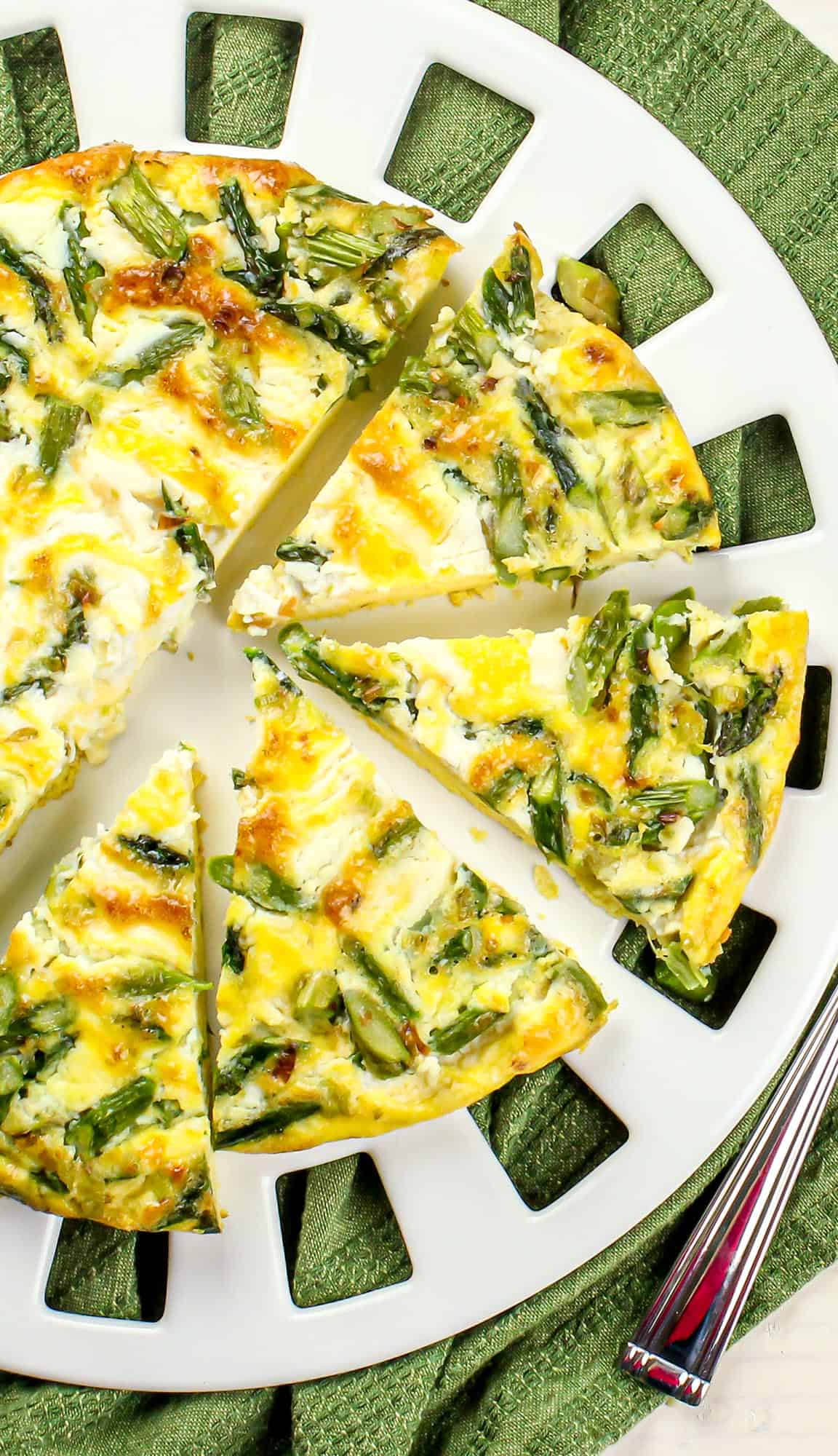 Asparagus and cheese frittata sliced on a white plate with green cloth and silver fork.