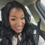Smiling woman with long black hair wearing seatbelt, sitting inside a car.