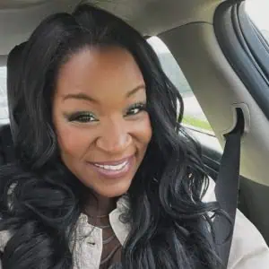 Smiling woman with long black hair wearing seatbelt, sitting inside a car.