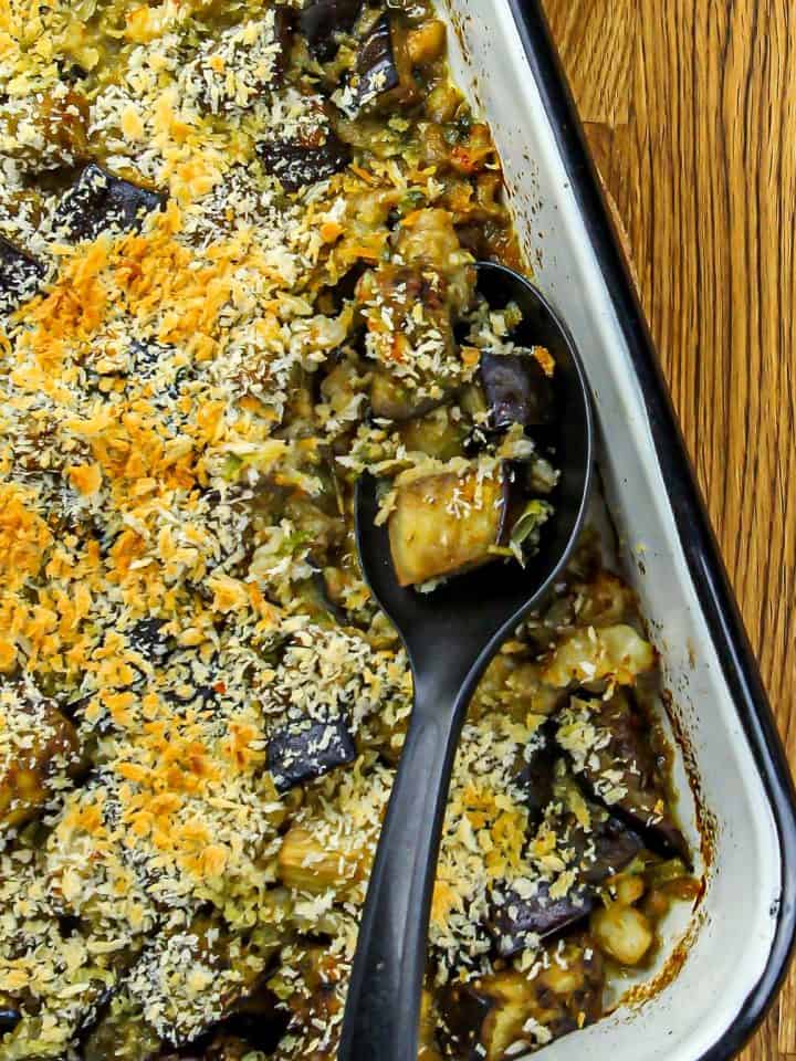 Baked eggplant and shrimp casserole topped with toasted breadcrumbs in a white enamel tray with a black serving spoon.