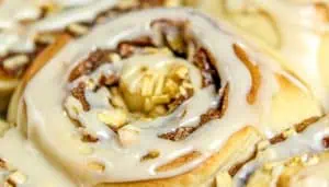 Close-up of cinnamon roll with icing and chopped apples on top.