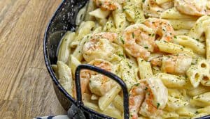 Shrimp pasta with creamy sauce and herbs in a black handle pan on a wooden surface.