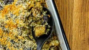 Baked eggplant and shrimp casserole with a crispy breadcrumb topping in a white roasting pan, spoon lifting a portion.