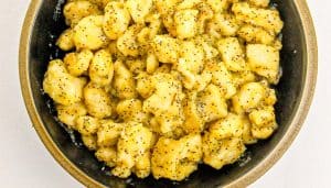 Black bowl filled with bite-sized chicken pieces coated in a light sticky sauce with black pepper flakes.