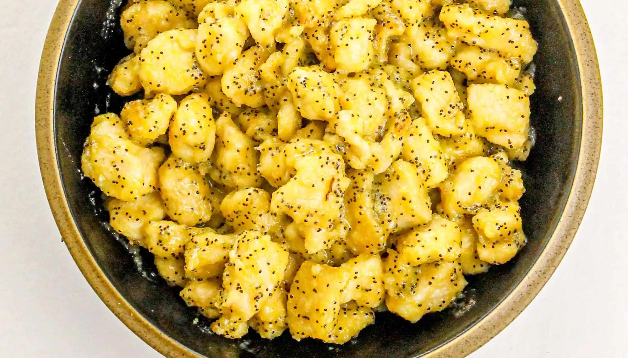 Black bowl filled with bite-sized chicken pieces coated in a light sticky sauce with black pepper flakes.