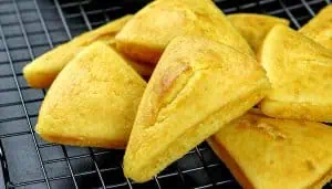 Golden triangular cornbread scones cooling on a black wire rack.