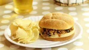 Sloppy Joe sandwich with ground turkey and black beans on a bun, served with ridged potato chips on a white plate.