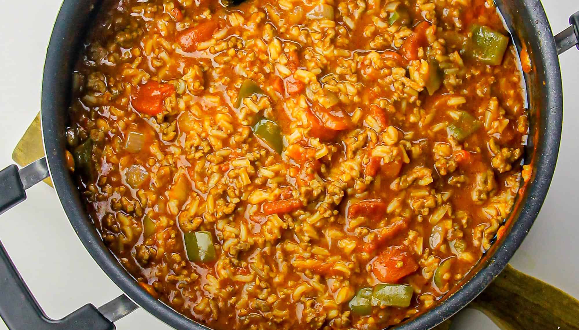 Pot of stuffed pepper soup with ground meat, rice, diced carrots, green bell peppers, and tomato-based sauce.