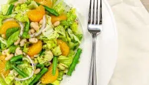 Salad with lettuce, mandarin orange slices, green beans, white beans, and red onion on a white plate with a fork on the side.