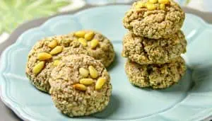 Six round cookies with pine nuts on top, on a light blue plate, with three cookies stacked and three side by side.