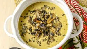 Creamy mushroom soup garnished with sautéed mushroom slices in a white bowl next to a patterned red and green cloth napkin.