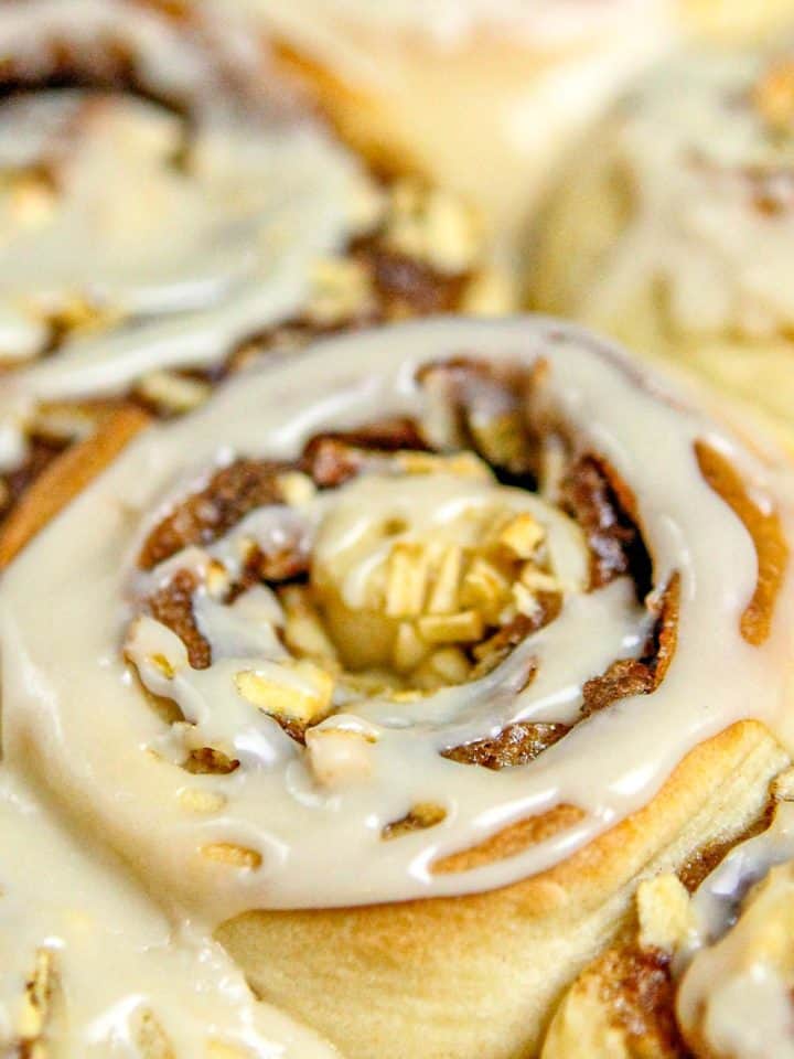 Close-up of cinnamon rolls topped with creamy icing and chopped apples.