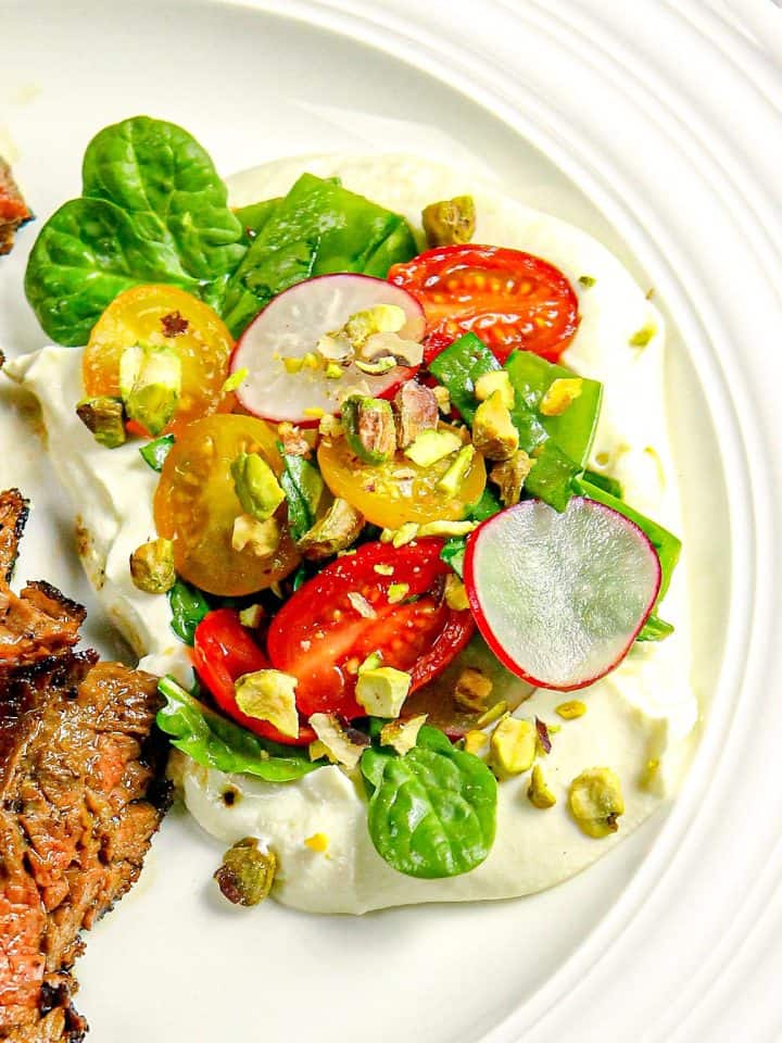 Sliced grilled steak on white plate with cherry tomatoes, spinach, radish slices, pistachios, and whipped ricotta cheese.