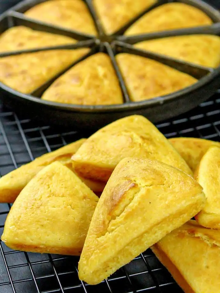 Golden triangular cornbread pieces cooling on a wire rack with a partially visible round cornbread pan in the background.