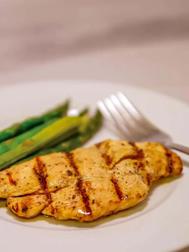 Grilled chicken breast with asparagus on a white plate, accompanied by a fork.