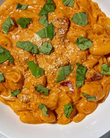 Gnocchi in creamy palomino sauce topped with chopped basil and grated Parmesan in a white bowl on marble surface.