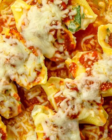 Baked pasta shells stuffed with cheese, topped with marinara sauce and melted mozzarella in a glass baking dish.
