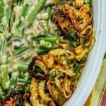 Green bean casserole topped with crispy fried onions in a white dish next to a yellow, green, and red striped napkin.