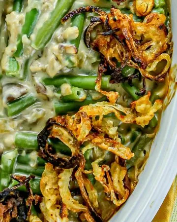 Green bean casserole topped with crispy fried onions in a white dish next to a yellow, green, and red striped napkin.