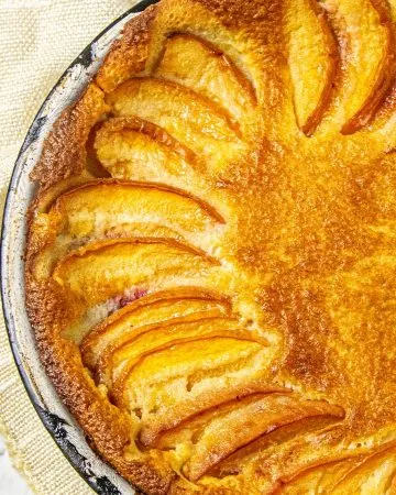 Golden brown baked tart with arranged fruit slices, set on a beige cloth and marble surface.