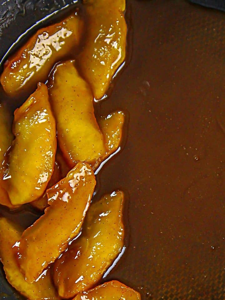 Caramelized apple slices cooking in a pan with glossy brown syrup.