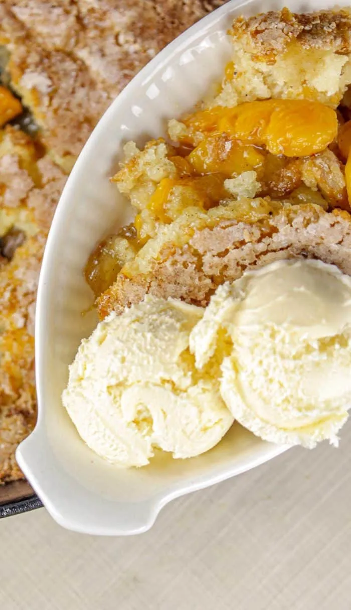 Peach cobbler served with two scoops of vanilla ice cream in a white dish.