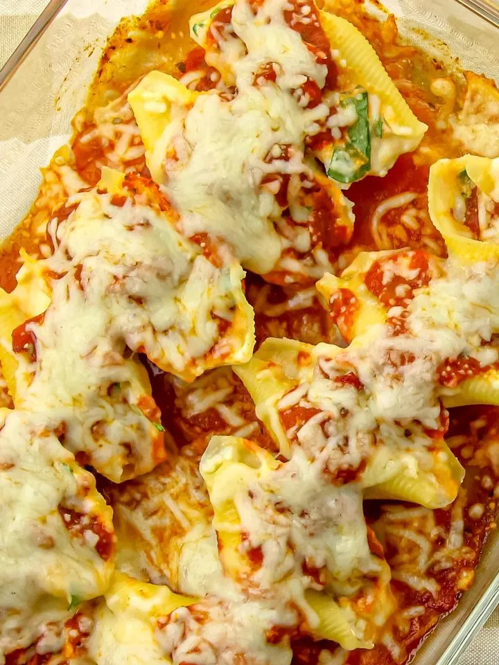 Stuffed pasta shells topped with melted cheese and tomato sauce in a glass baking dish on a striped surface.