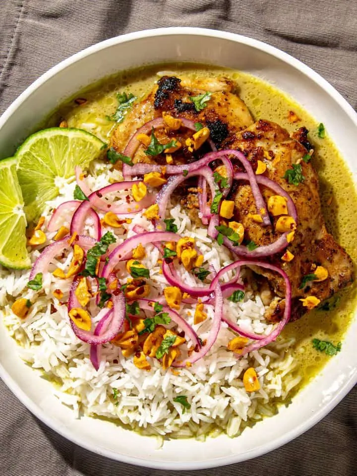 Grilled chicken thigh served with white rice, pickled red onions, toasted garlic, cilantro, and lime wedges in green sauce.