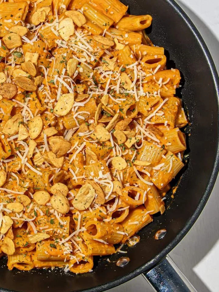 Rigatoni pasta in creamy gochujang sauce topped with garlic chips, grated cheese, and parsley in a black skillet.
