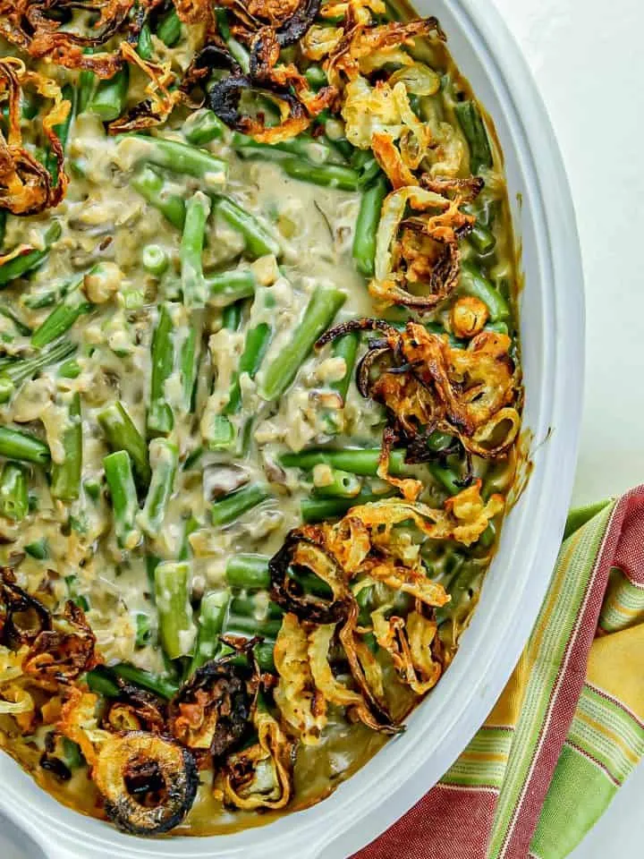 Green bean casserole topped with crispy fried onions in a white baking dish on a colorful striped cloth.