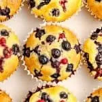 Blueberry muffins with visible whole blueberries, in white paper liners, arranged on a white background.