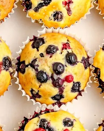 Blueberry muffins with visible whole blueberries, in white paper liners, arranged on a white background.
