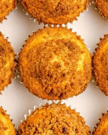 Nine golden brown crumb-topped muffins arranged in three rows on a white background.
