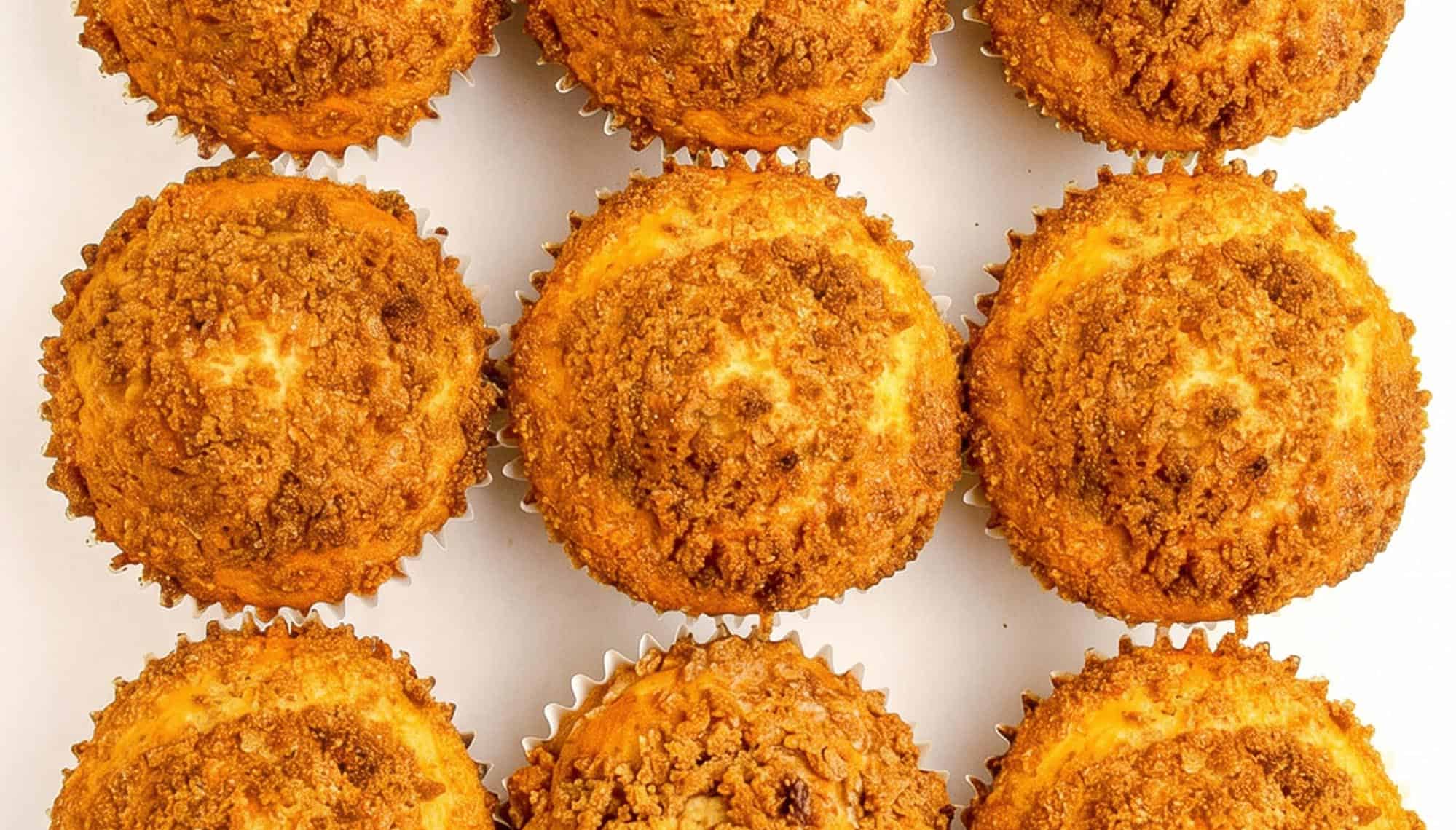 Nine golden brown crumb-topped muffins arranged in three rows on a white background.