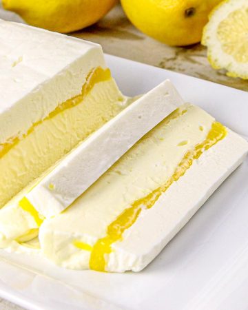 Lemon semifreddo dessert with two slices cut, placed on a white rectangular plate, garnished with fresh lemon slices and whole lemons.