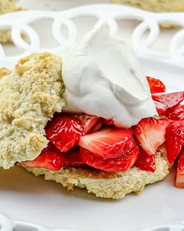 Biscuit split open with sliced strawberries and whipped cream on a white decorative plate.