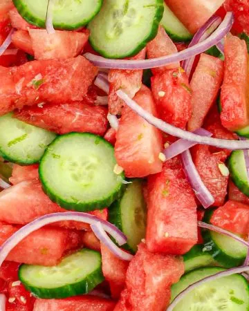 Watermelon, cucumber slices, and thin red onion strips in a clear bowl.
