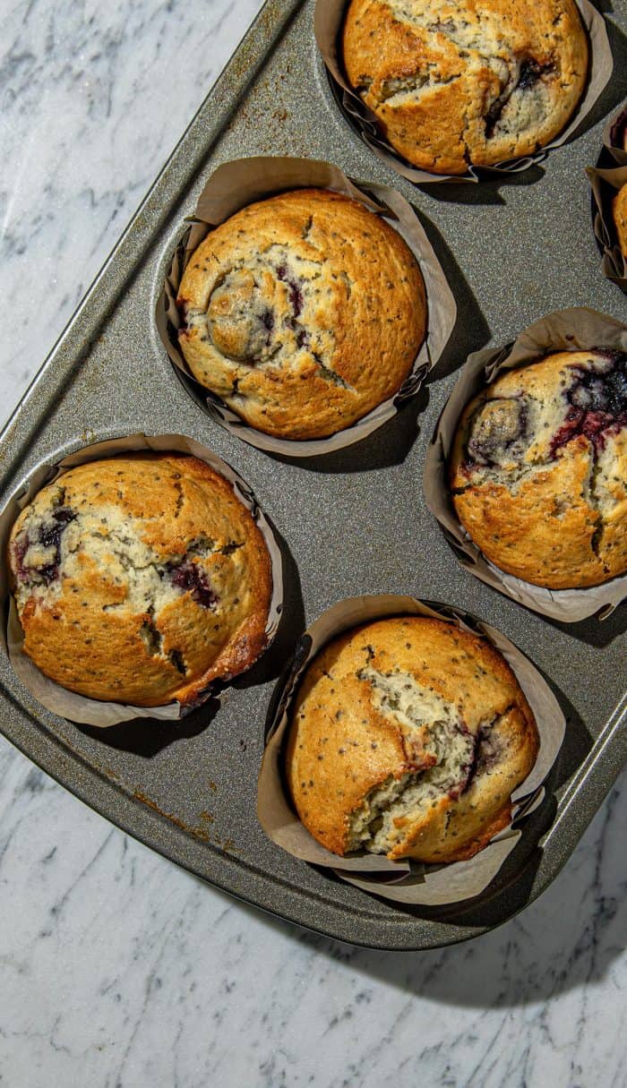 Golden cherry chia muffins with cracked tops in parchment cups on a baking tray over a marble surface.