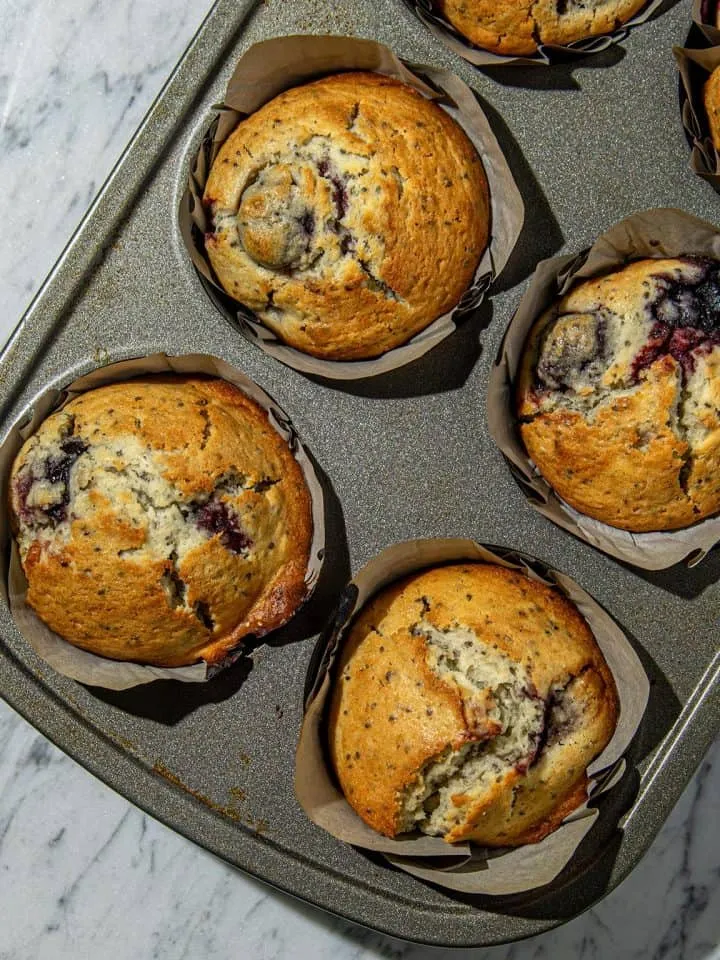 Golden cherry chia muffins with cracked tops in parchment cups on a baking tray over a marble surface.