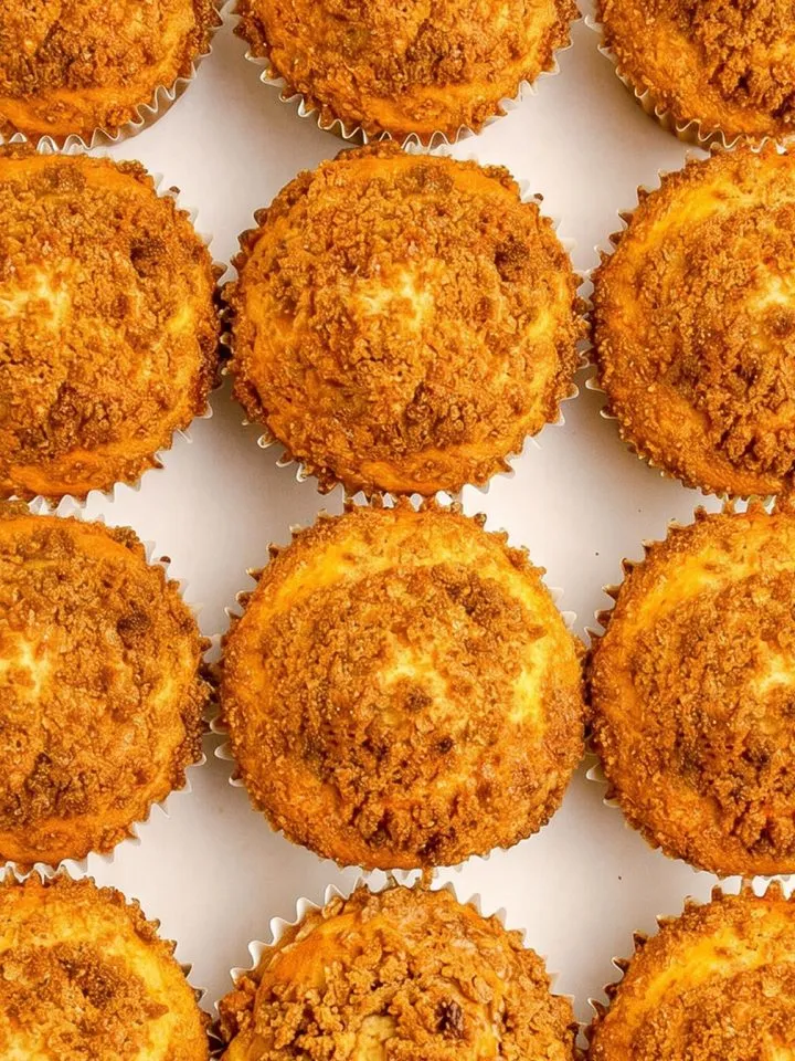 Twelve golden-brown muffins with crumbly streusel topping arranged in a grid on a white surface.