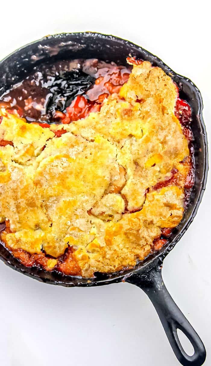 Peach cobbler with golden crust in a black cast iron skillet on a white surface.