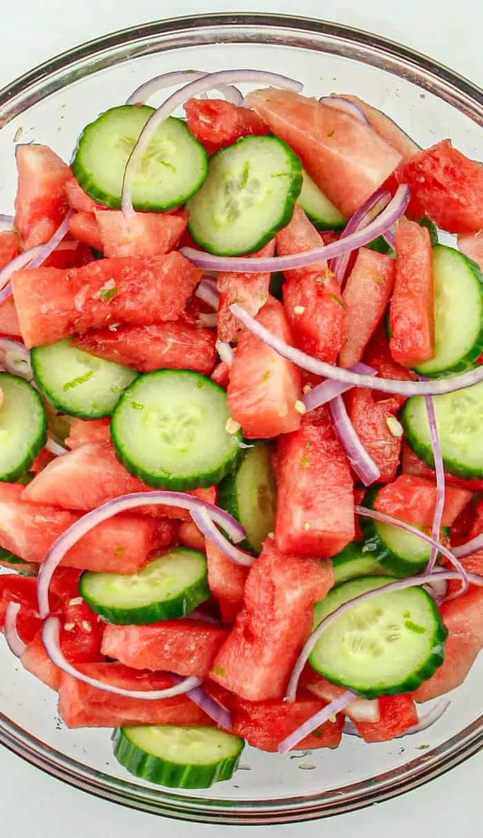 Watermelon, cucumber slices, and thin red onion strips in a glass bowl.