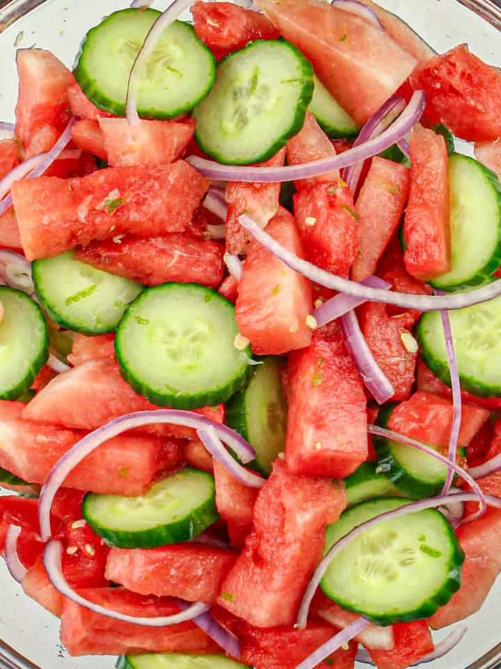 Watermelon, cucumber slices, and thin red onion strips in a glass bowl.